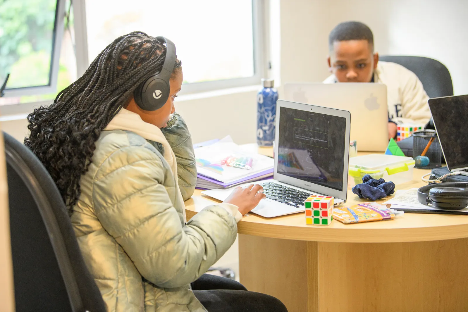 Two students working independently on laptops at a shared table