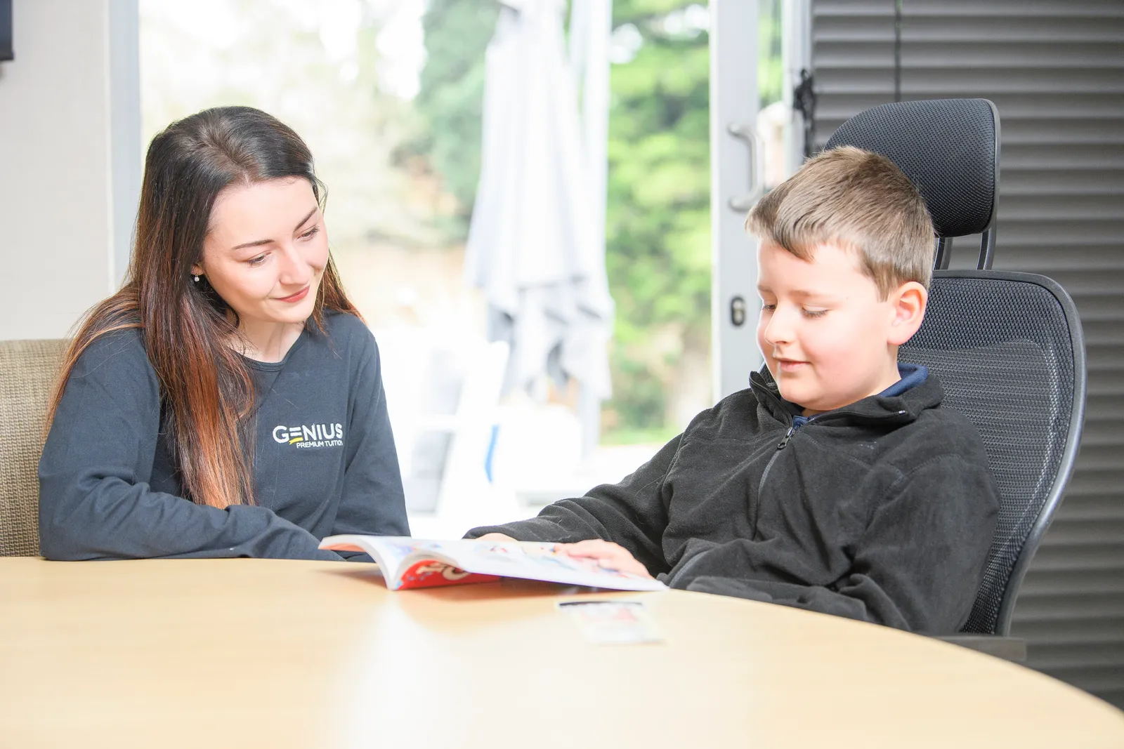 A Genius tutor and young learner smiling together over an open workbook